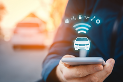 A man holding a phone with icons above the screen, relating to telematics for a car in the background